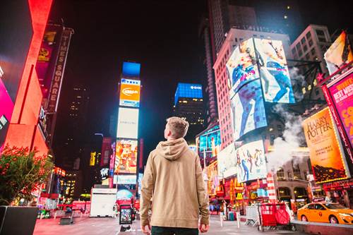 Junger Mann steht in New York und schaut nachts auf Werbebanner